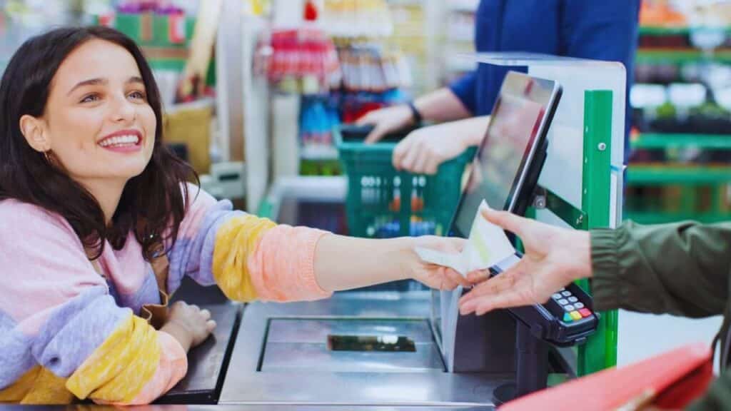 Smiling female cashier giving receipt to customer at supermarket checkout