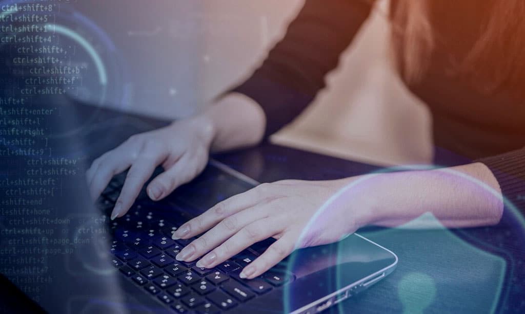 Hands typing on a laptop with cybersecurity symbols and code. 