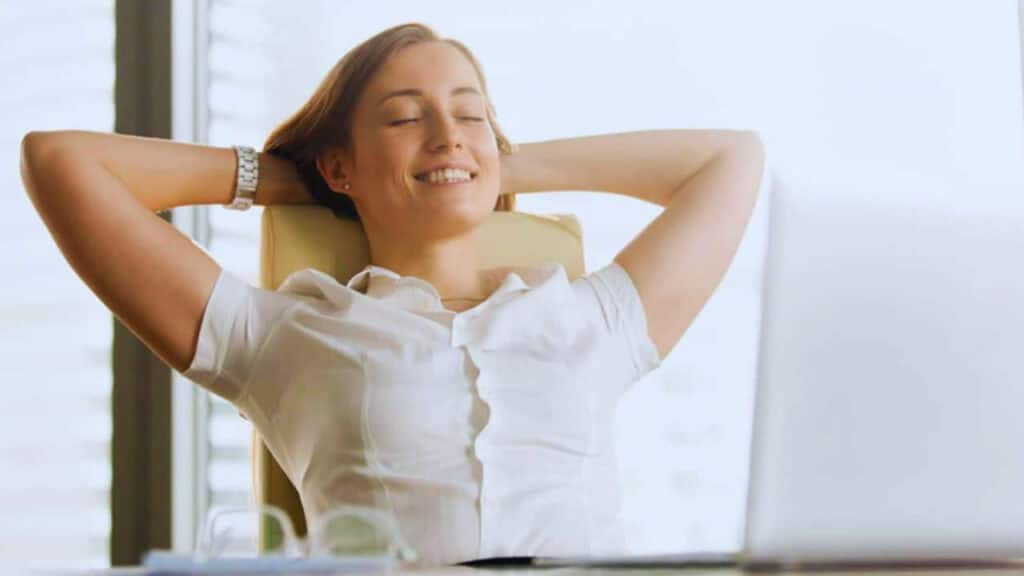 Smiling woman relaxing with her hands behind her head while sitting at a desk.