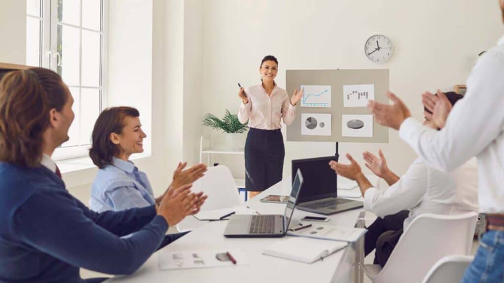Team applauding a woman presenting graphs during a meeting in a bright office.