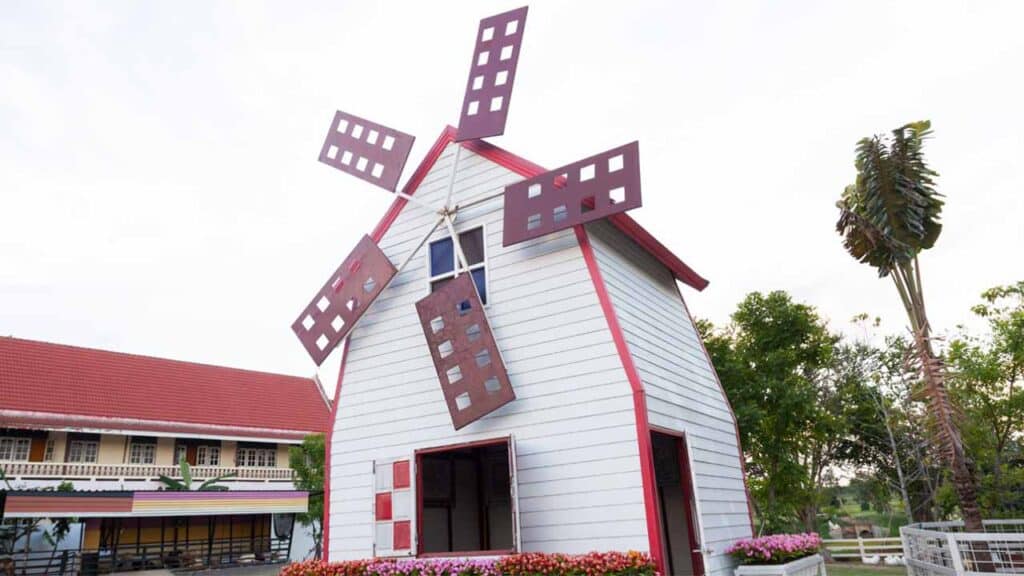 Small windmill with red blades and white walls in a garden setting