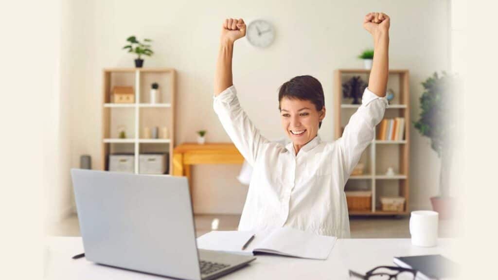 Excited woman celebrating success while working on a laptop in a home office.