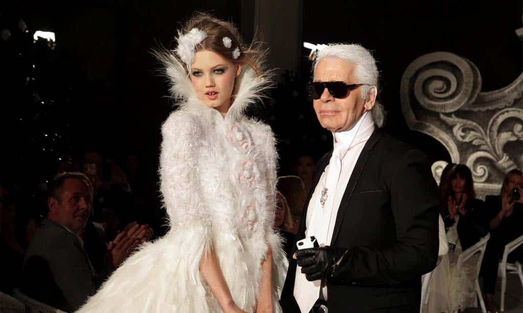 Karl Lagerfeld with a model in a white feathered dress at a fashion show.