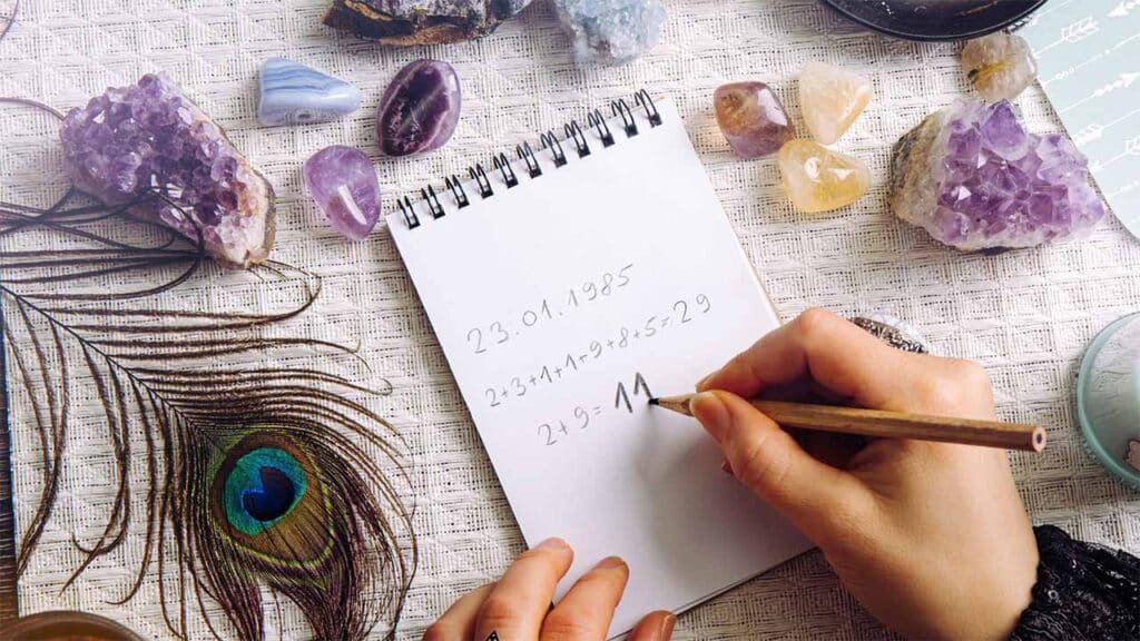 A person writes numerology calculations in a notebook surrounded by healing crystals