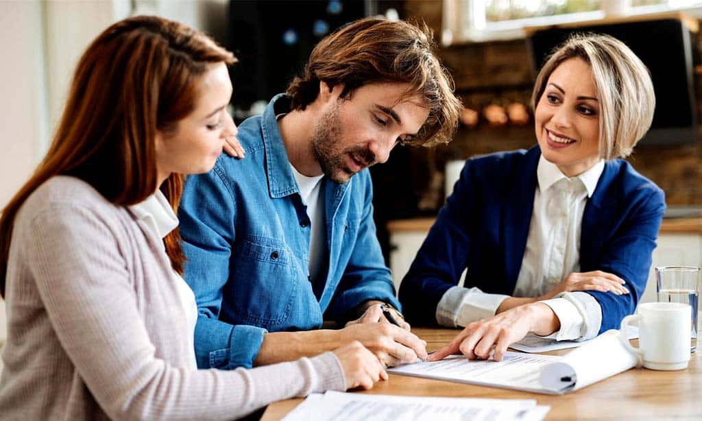 Couple signing a contract with a real estate agent, finalizing a property deal, and discussing terms