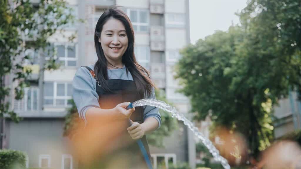 Smiling woman watering plants with a hose in a garden